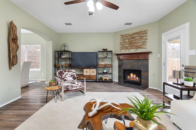 living room featuring a tiled fireplace, ceiling fan, and dark hardwood / wood-style flooring