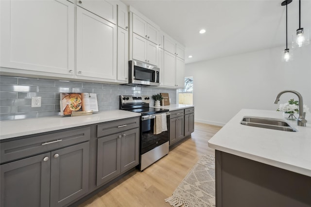 kitchen with stainless steel appliances, gray cabinetry, decorative backsplash, light wood-style floors, and a sink