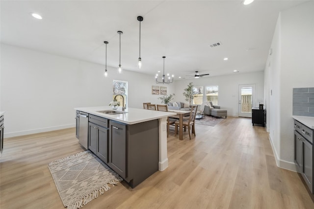 kitchen featuring light wood finished floors, light countertops, open floor plan, a sink, and dishwasher