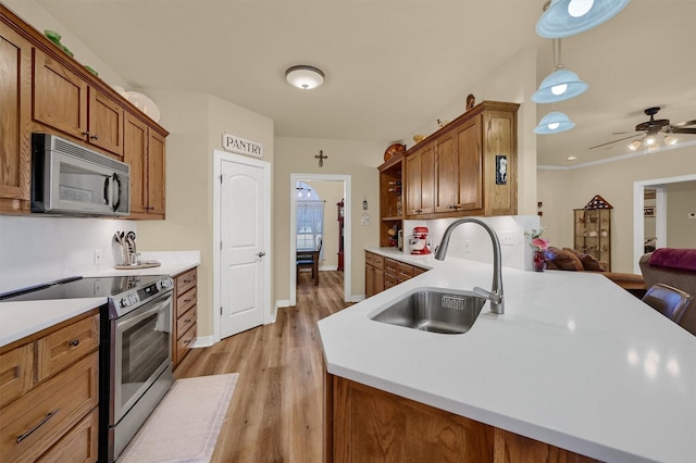 kitchen with appliances with stainless steel finishes, sink, hanging light fixtures, kitchen peninsula, and light hardwood / wood-style flooring