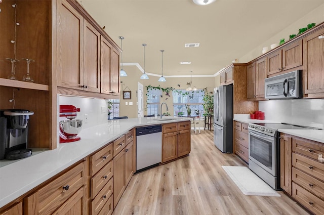 kitchen with appliances with stainless steel finishes, decorative light fixtures, sink, ornamental molding, and light wood-type flooring