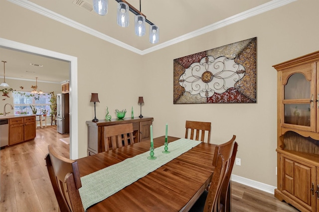 dining space with sink, light hardwood / wood-style floors, an inviting chandelier, and crown molding