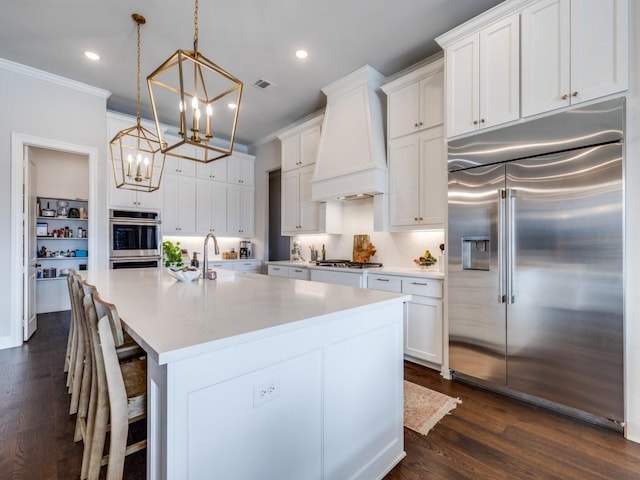 kitchen with stainless steel appliances, premium range hood, white cabinetry, and decorative light fixtures