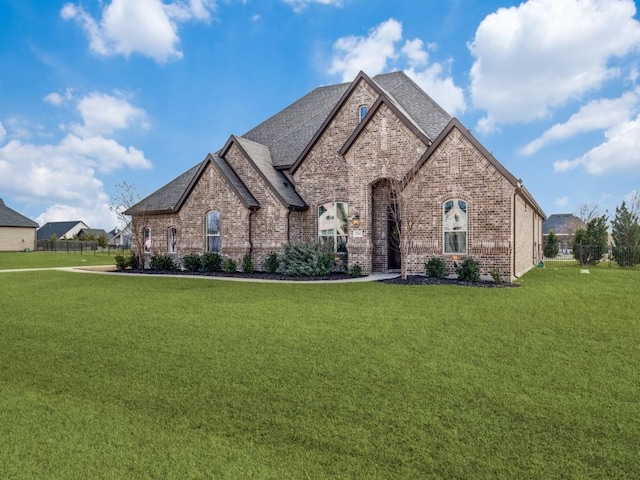 french provincial home featuring brick siding, roof with shingles, a front lawn, and fence