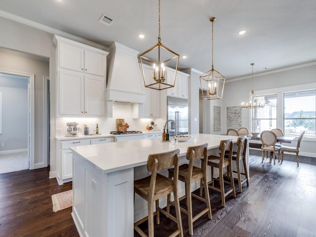 kitchen with hanging light fixtures, white cabinets, custom range hood, and a large island with sink