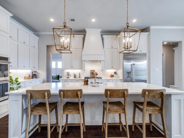 kitchen featuring built in fridge, a large island with sink, and premium range hood