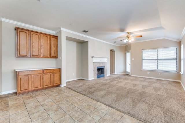 unfurnished living room featuring lofted ceiling, crown molding, ceiling fan, light colored carpet, and a tiled fireplace