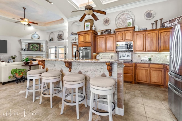 kitchen featuring appliances with stainless steel finishes, a kitchen bar, an island with sink, decorative backsplash, and ceiling fan