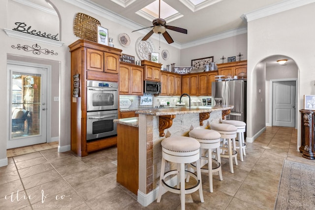 kitchen featuring coffered ceiling, ornamental molding, stainless steel appliances, and an island with sink