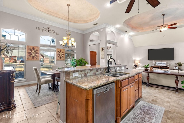 kitchen with pendant lighting, a tray ceiling, an island with sink, sink, and stainless steel dishwasher