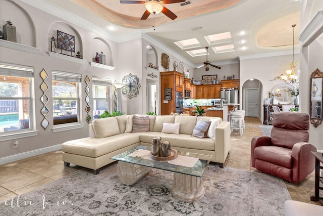 living room with a skylight, ceiling fan with notable chandelier, light tile patterned floors, and a tray ceiling