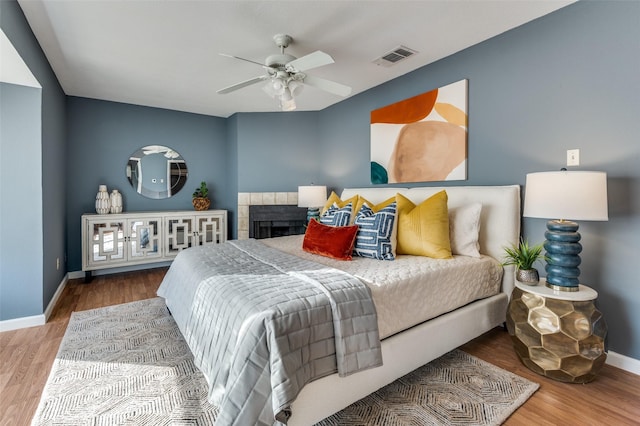 bedroom with wood-type flooring, a tile fireplace, and ceiling fan