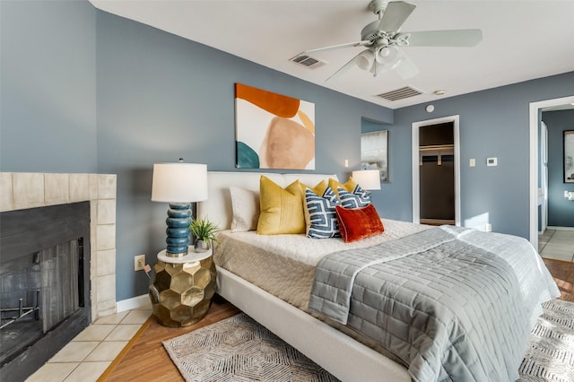 bedroom featuring a spacious closet, a closet, ceiling fan, light hardwood / wood-style flooring, and a tiled fireplace