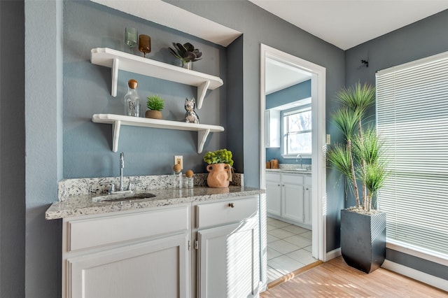 bar featuring sink, white cabinets, and light stone countertops