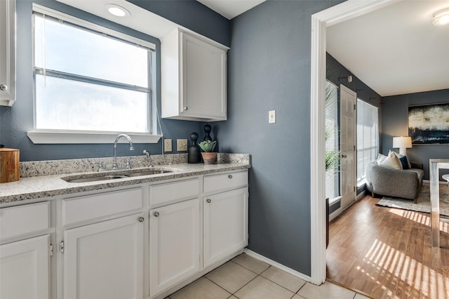 kitchen featuring sink, white cabinetry, light tile patterned floors, and light stone countertops