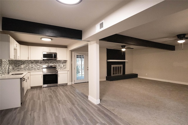 kitchen featuring sink, white cabinetry, a large fireplace, beamed ceiling, and stainless steel appliances