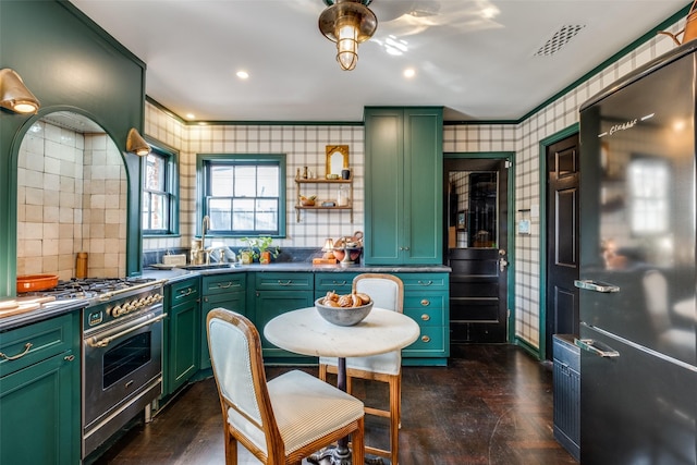 kitchen with green cabinetry, dark parquet floors, black fridge, and high end stainless steel range