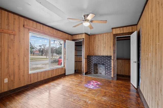 unfurnished living room featuring dark wood-type flooring, crown molding, a brick fireplace, and wood walls