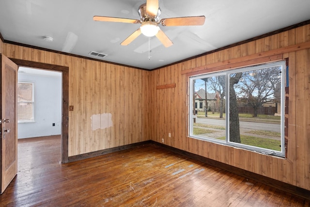 unfurnished room with wood-type flooring, ceiling fan, crown molding, and wood walls