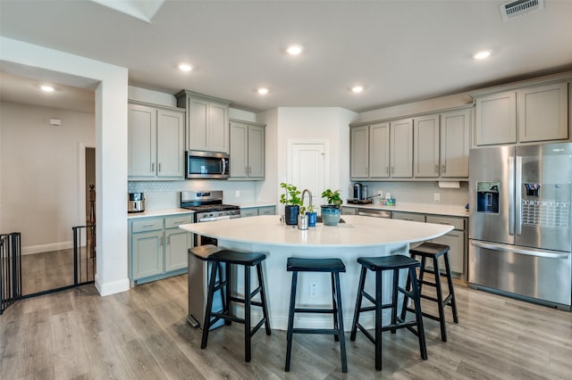 kitchen featuring light hardwood / wood-style floors, a kitchen breakfast bar, decorative backsplash, and appliances with stainless steel finishes