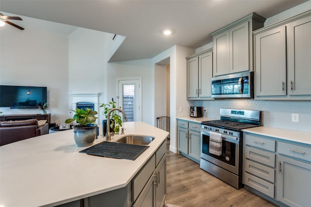 kitchen with gray cabinetry, stainless steel appliances, tasteful backsplash, sink, and a center island with sink