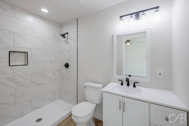 bathroom with a tile shower, toilet, and vanity