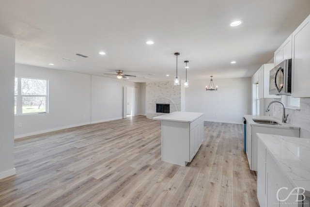 kitchen featuring white cabinets, a center island, sink, hanging light fixtures, and a brick fireplace