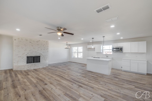 kitchen featuring a fireplace, white cabinets, sink, light hardwood / wood-style flooring, and ceiling fan