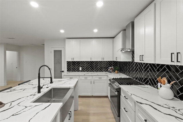 kitchen featuring wall chimney range hood, white cabinetry, light stone counters, and stainless steel gas stove