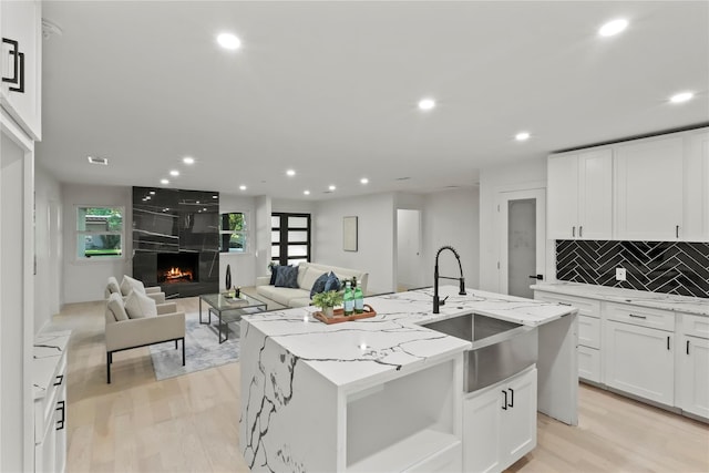 kitchen with sink, a center island with sink, white cabinetry, and light stone countertops