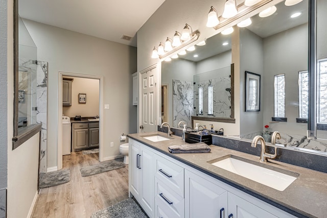 bathroom with tiled shower, toilet, vanity, hardwood / wood-style flooring, and washer / clothes dryer