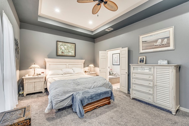 carpeted bedroom with crown molding, a raised ceiling, ceiling fan, and ensuite bathroom