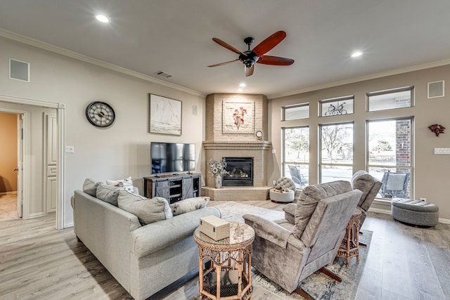 living room featuring crown molding, a large fireplace, ceiling fan, and light hardwood / wood-style flooring