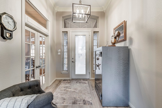 entryway with a notable chandelier, crown molding, light hardwood / wood-style floors, and french doors