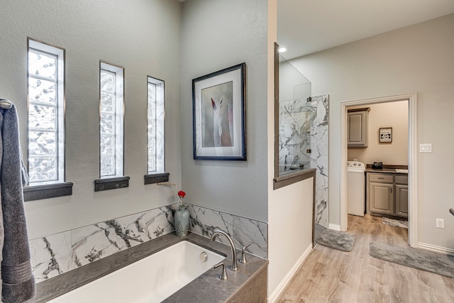 bathroom featuring washer / clothes dryer, hardwood / wood-style floors, shower with separate bathtub, and a wealth of natural light