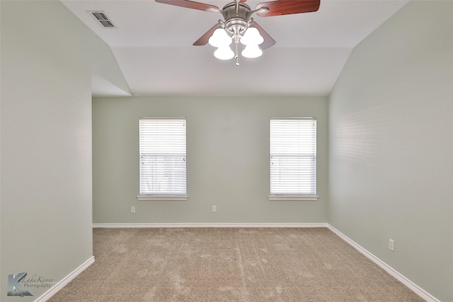 carpeted spare room featuring a healthy amount of sunlight, vaulted ceiling, and ceiling fan