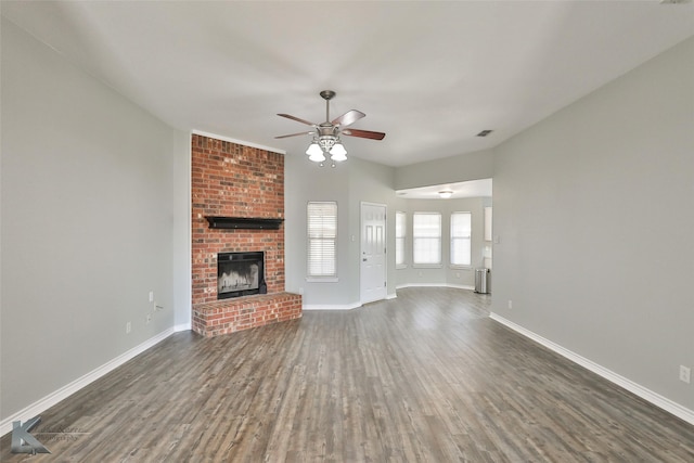 unfurnished living room featuring ceiling fan, dark wood-type flooring, and a brick fireplace