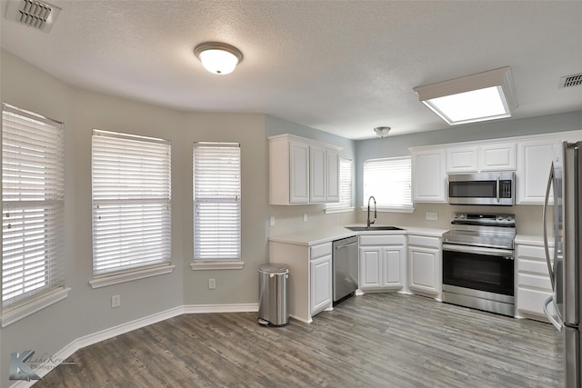 kitchen featuring a textured ceiling, sink, white cabinets, light hardwood / wood-style flooring, and stainless steel appliances