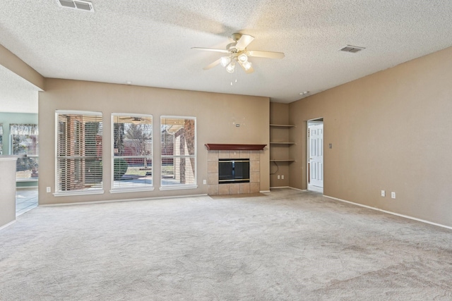 unfurnished living room with ceiling fan, a tiled fireplace, light carpet, and built in features