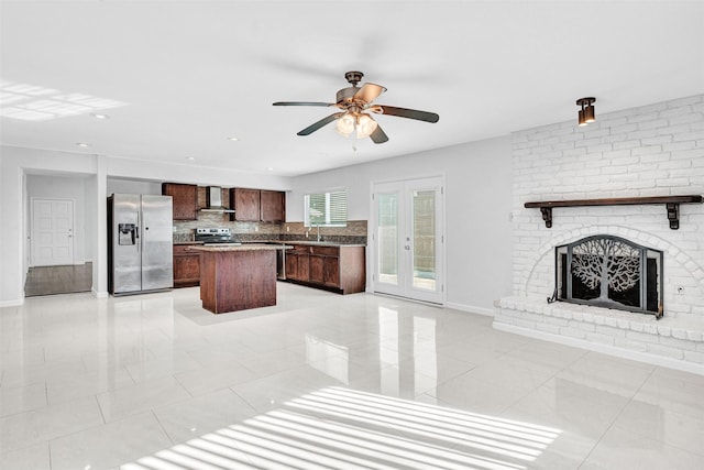 kitchen featuring ceiling fan, appliances with stainless steel finishes, a kitchen island, decorative backsplash, and wall chimney exhaust hood