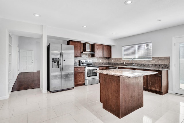 kitchen with appliances with stainless steel finishes, sink, a center island, light stone counters, and wall chimney exhaust hood