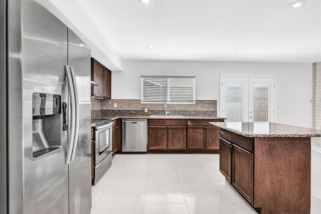 kitchen with sink, appliances with stainless steel finishes, backsplash, a center island, and light stone countertops