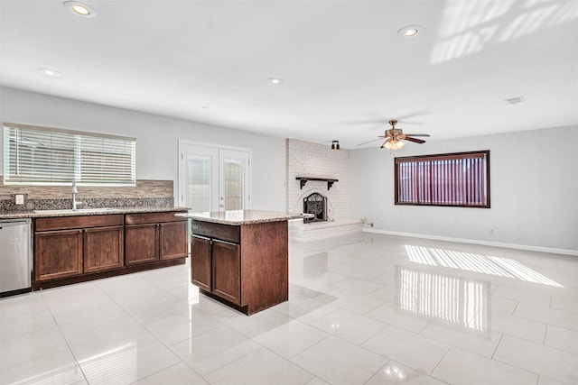 kitchen featuring dishwasher, sink, a center island, light stone countertops, and a brick fireplace