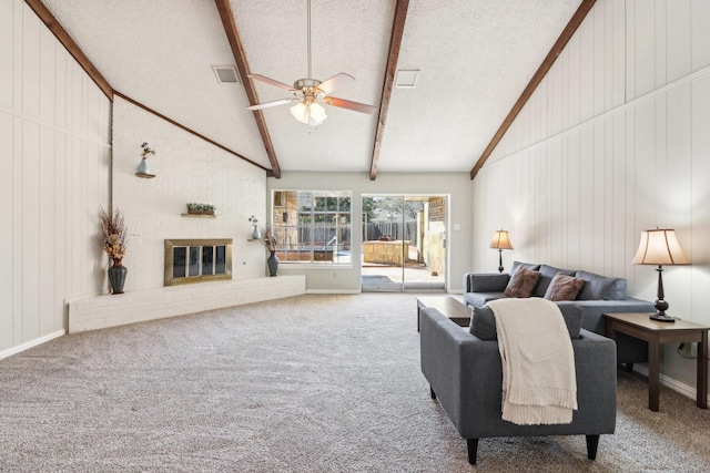 carpeted living room with a textured ceiling, wooden walls, a fireplace, ceiling fan, and beam ceiling