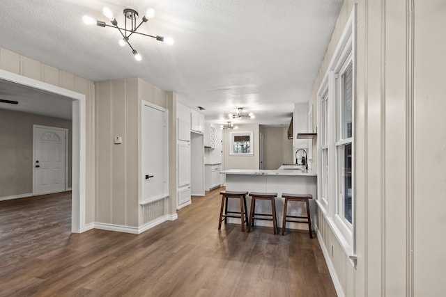 kitchen with kitchen peninsula, sink, white cabinets, dark hardwood / wood-style floors, and a breakfast bar area