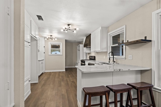 kitchen featuring kitchen peninsula, stainless steel range with gas stovetop, sink, white cabinets, and a breakfast bar