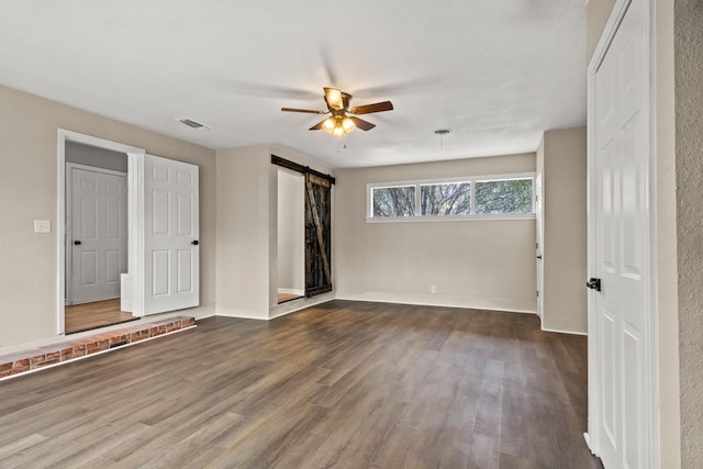 empty room featuring ceiling fan, dark wood-type flooring, and a barn door