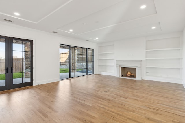 unfurnished living room with built in features, light wood-type flooring, a raised ceiling, and french doors