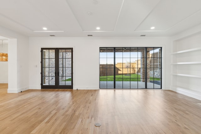 empty room featuring built in features, french doors, a raised ceiling, and light hardwood / wood-style floors