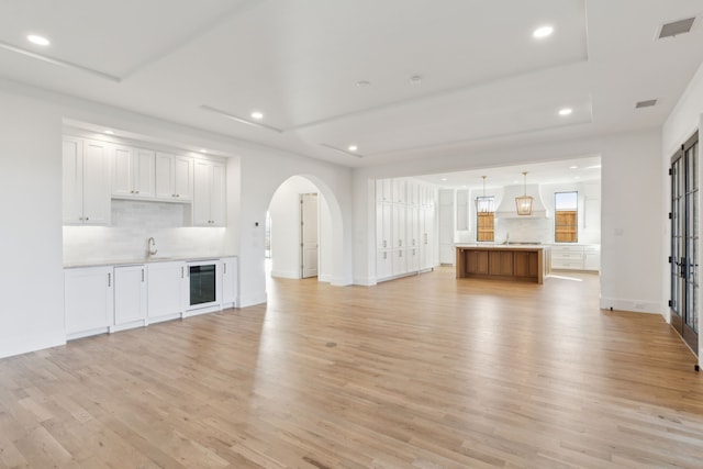 unfurnished living room featuring sink, a tray ceiling, light hardwood / wood-style flooring, and wine cooler